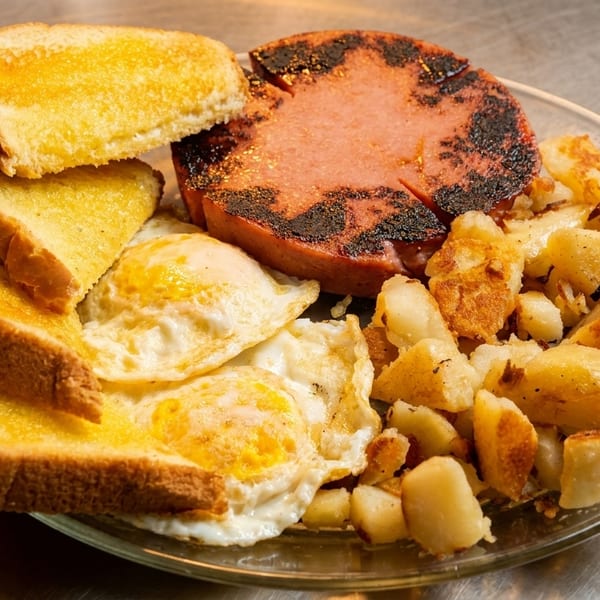 A breakfast plate with grilled bologna, fried eggs, home fries, and buttered toast.