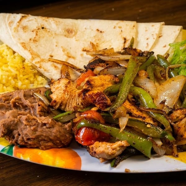 Chicken fajitas with grilled peppers and onions, rice, refried beans, tortillas, and a side salad.