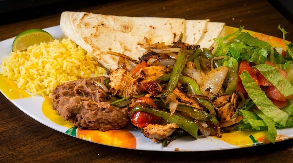 Chicken fajitas with grilled peppers and onions, rice, refried beans, tortillas, and a side salad.