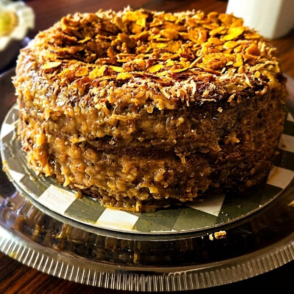 A German chocolate cake with coconut pecan frosting and toasted coconut flakes on a silver platter.