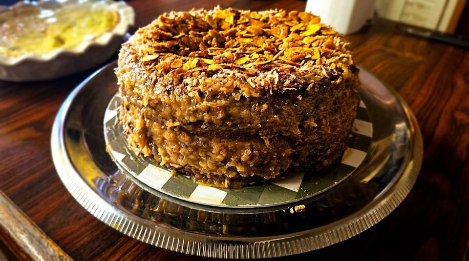 A German chocolate cake with coconut pecan frosting and toasted coconut flakes on a silver platter.