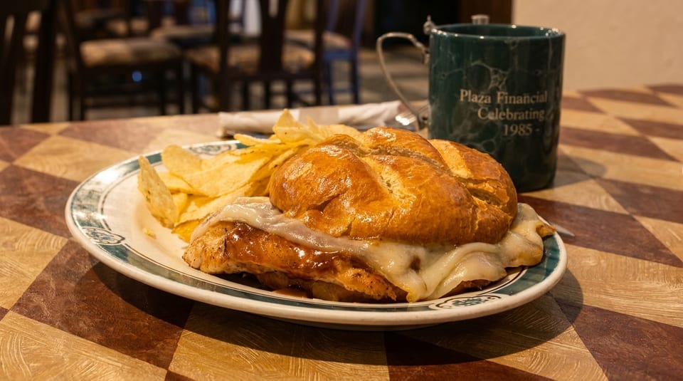 A chicken sandwich with melted cheese and chips on a plate, next to a green mug.