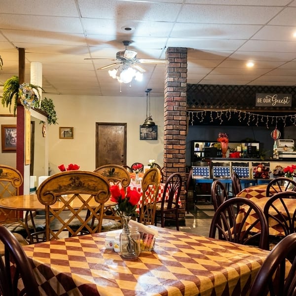 Cozy restaurant interior with checkered tablecloths, wooden chairs, and red roses on tables.