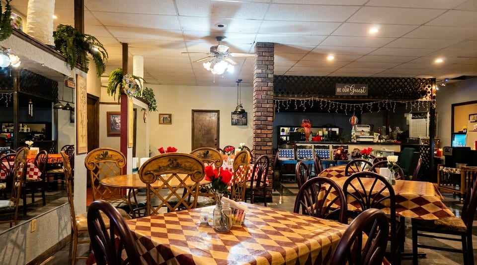 Cozy restaurant interior with checkered tablecloths, wooden chairs, and red roses on tables.